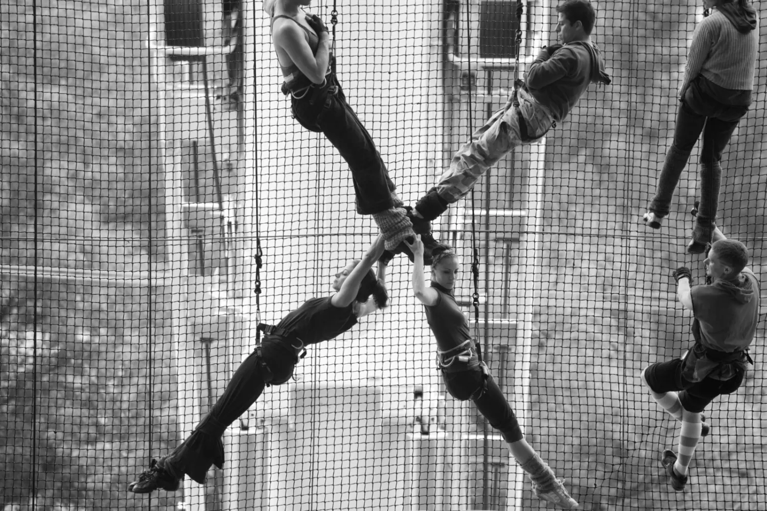 Bailarines escalando una red vertical sobre la fachada de un edificio