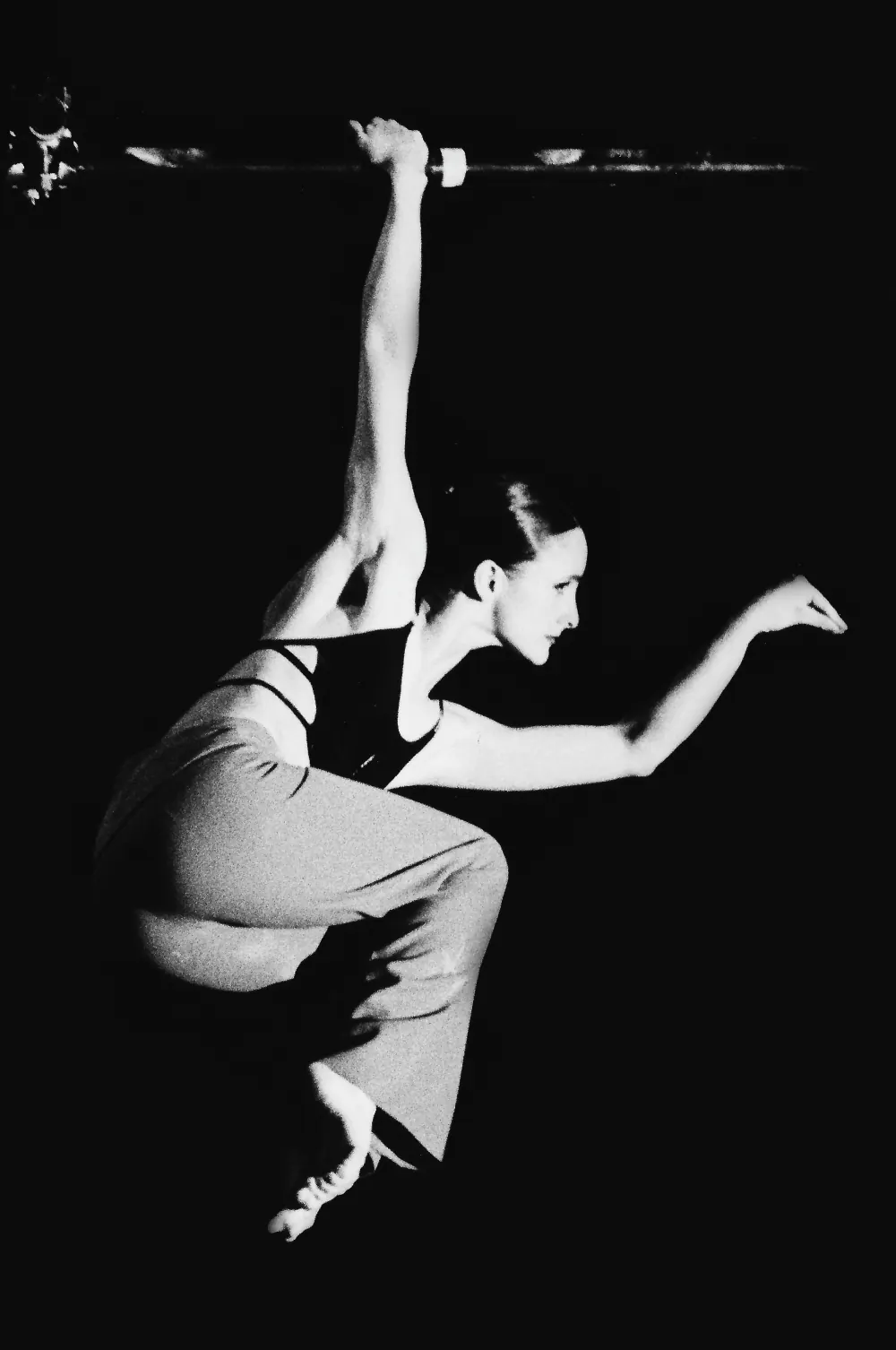 Bailarina colgada de una barra con un brazo, en posición de vuelo