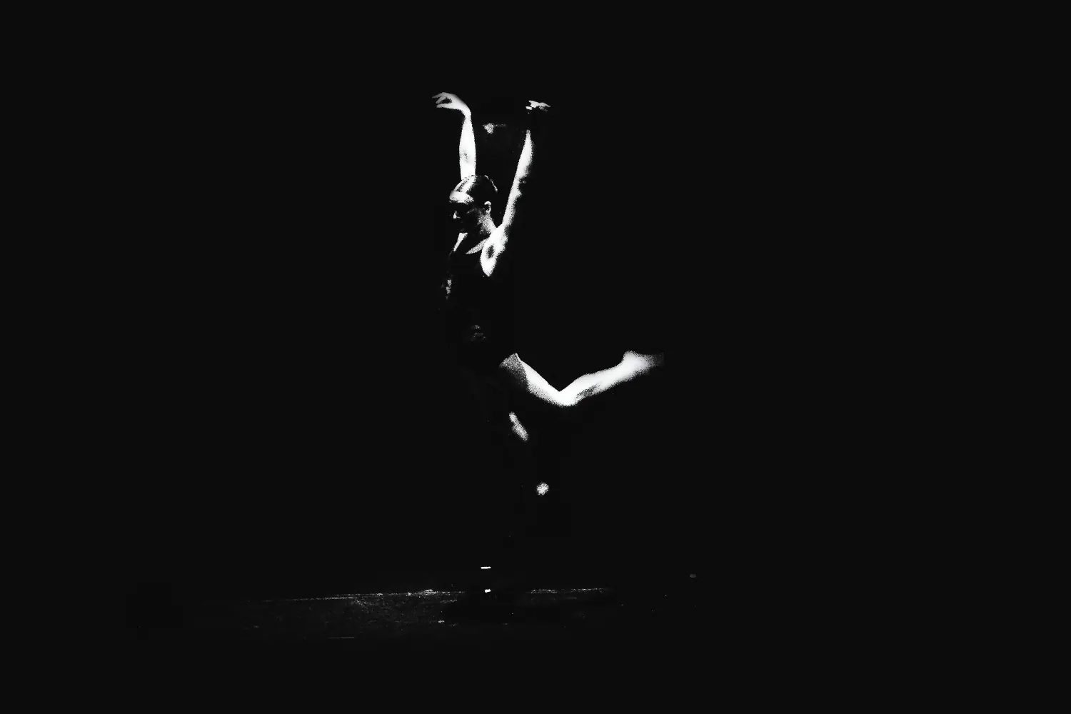 Silueta de una bailarina con los brazos en alto bajo un haz de luz